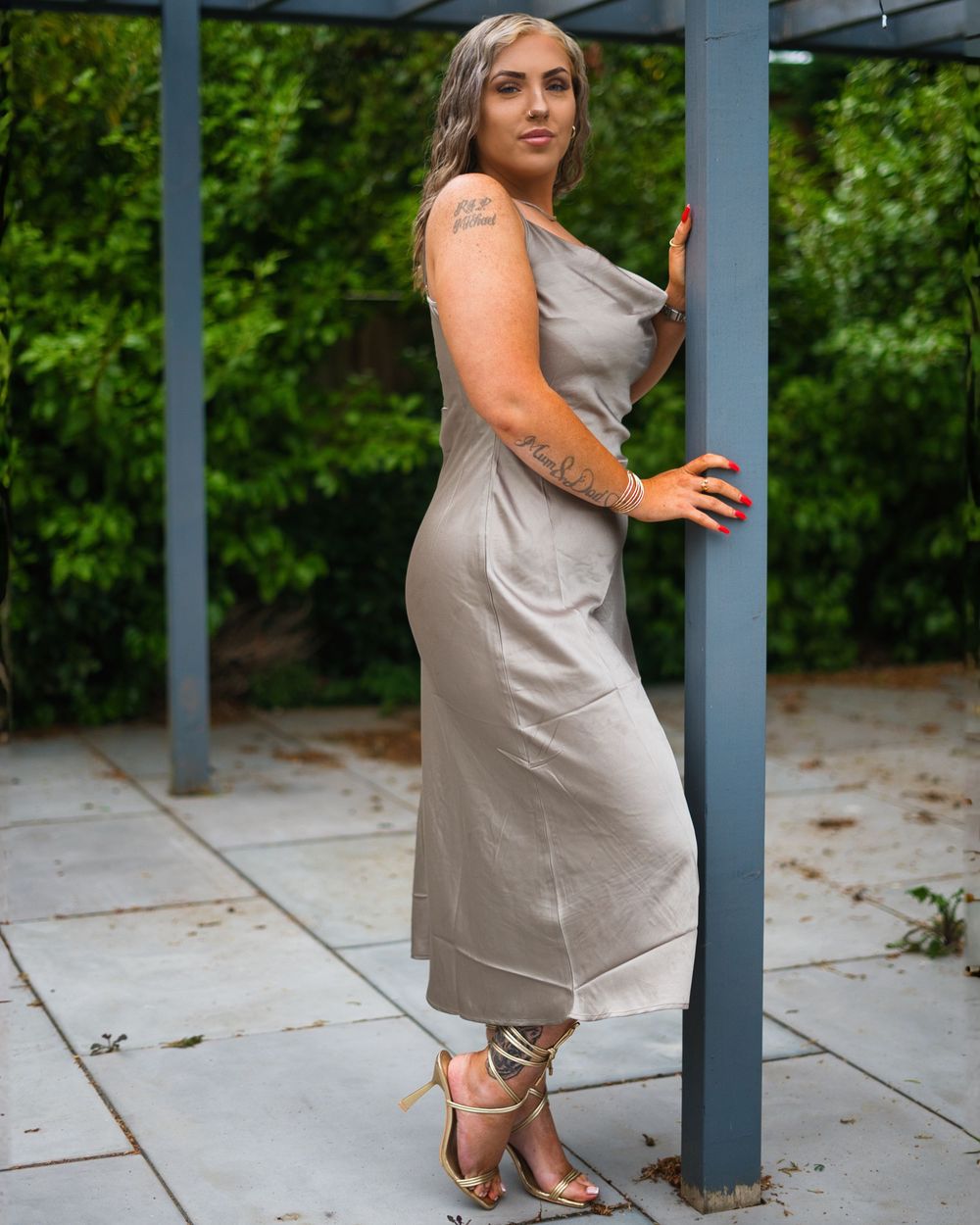 Woman in gray dress sits gracefully on outdoor patio with green foliage visible.