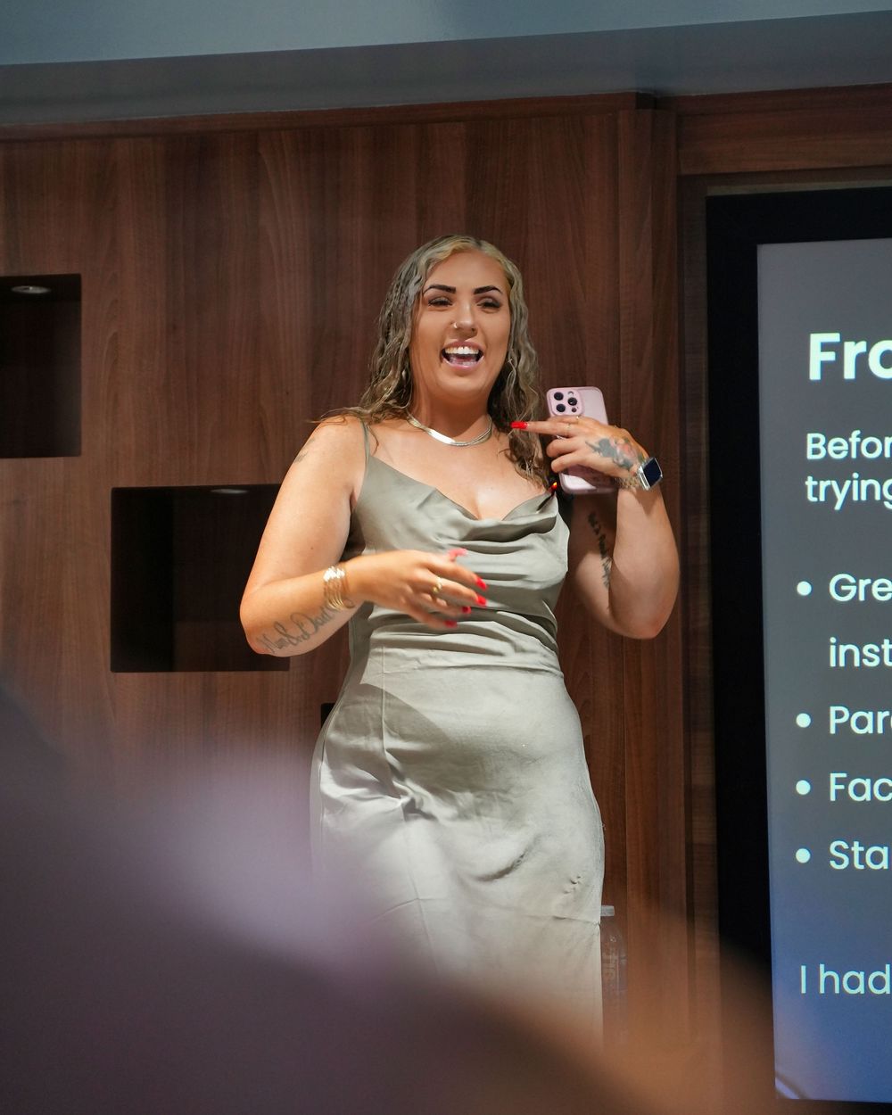 Person in gray top gestures while speaking in wood-paneled conference room.