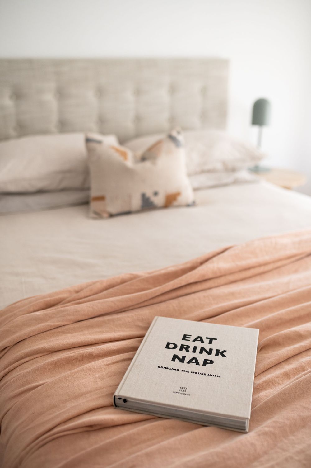 A minimalist bedroom setup with a book titled 'Eat Drink Nap' on light peach colored bedding.