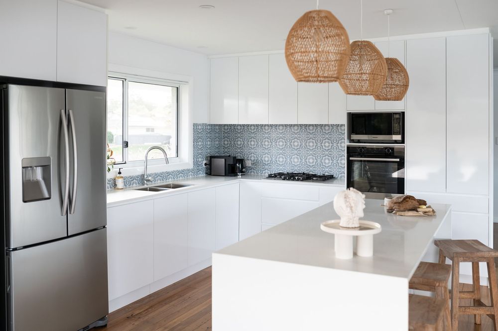 Modern white kitchen interior with sleek cabinetry, stainless steel appliances, and rattan pendant lights.