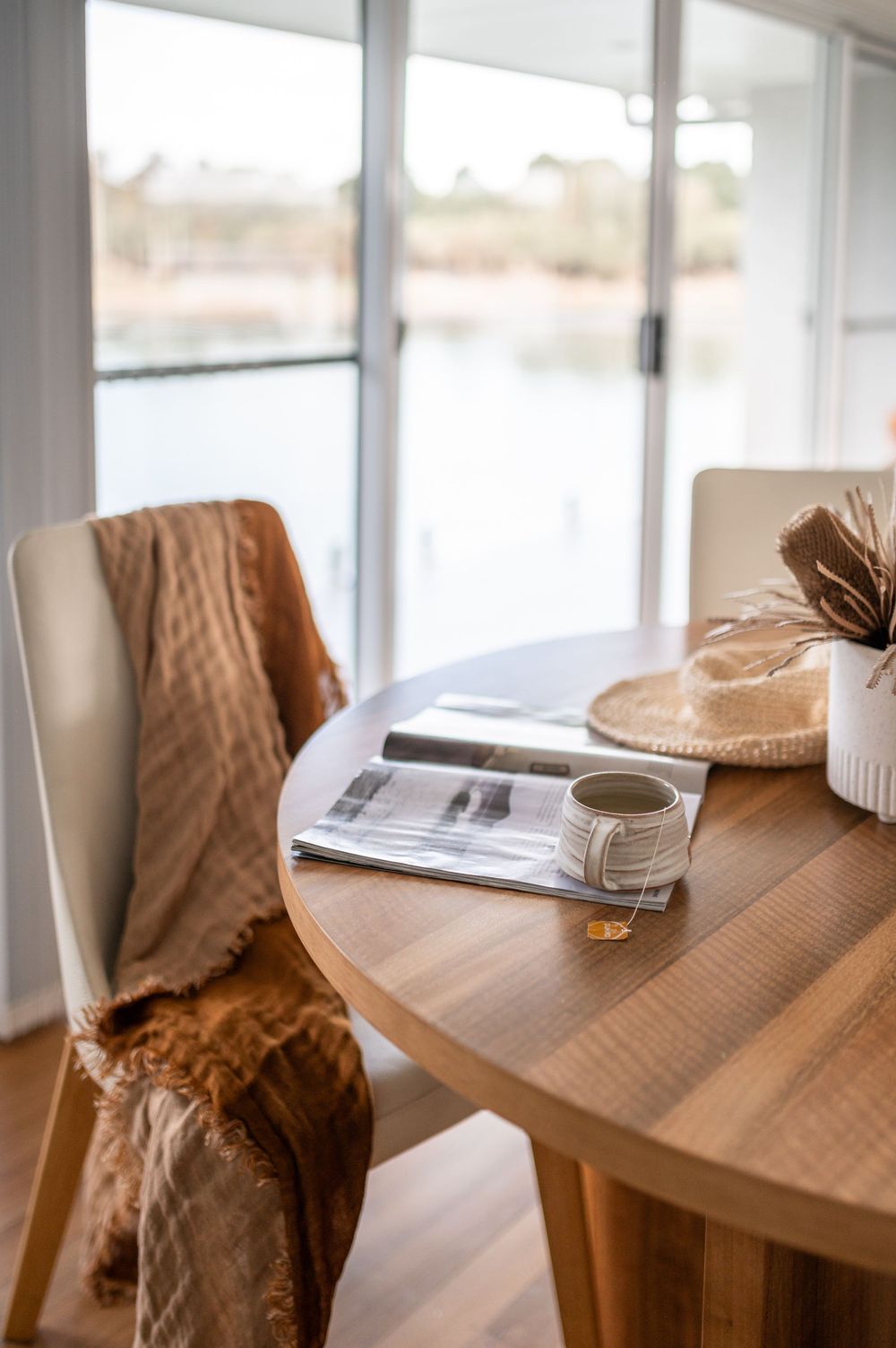 Modern wooden table with coffee cups and reading materials in a sunlit room with natural decor elements.