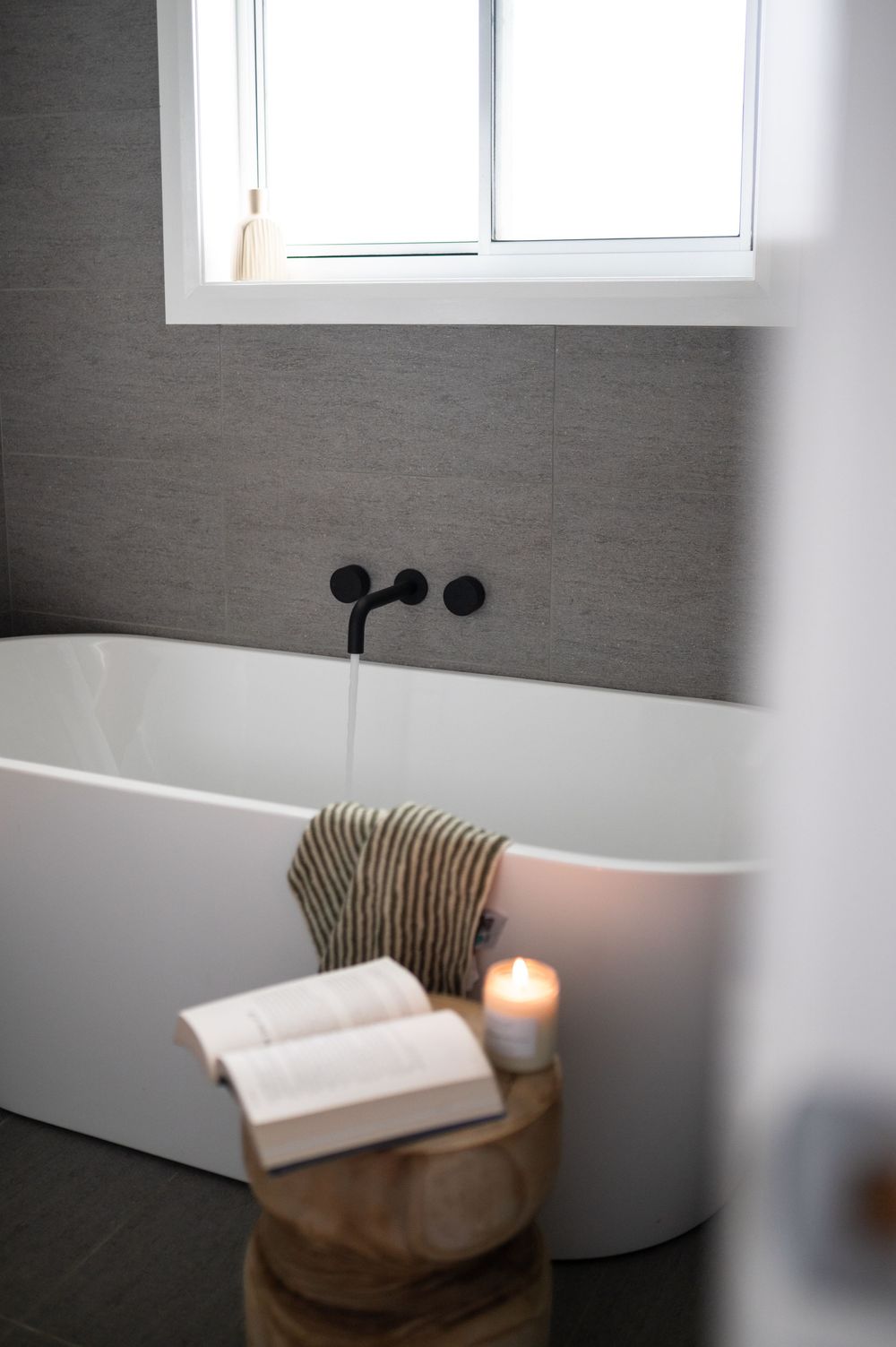 Serene bathroom interior with freestanding bathtub and striped bath pillow under window.