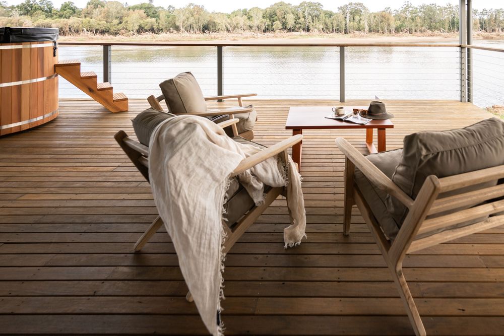 Modern lakeside deck with minimalist furniture overlooks calm water and natural landscape.