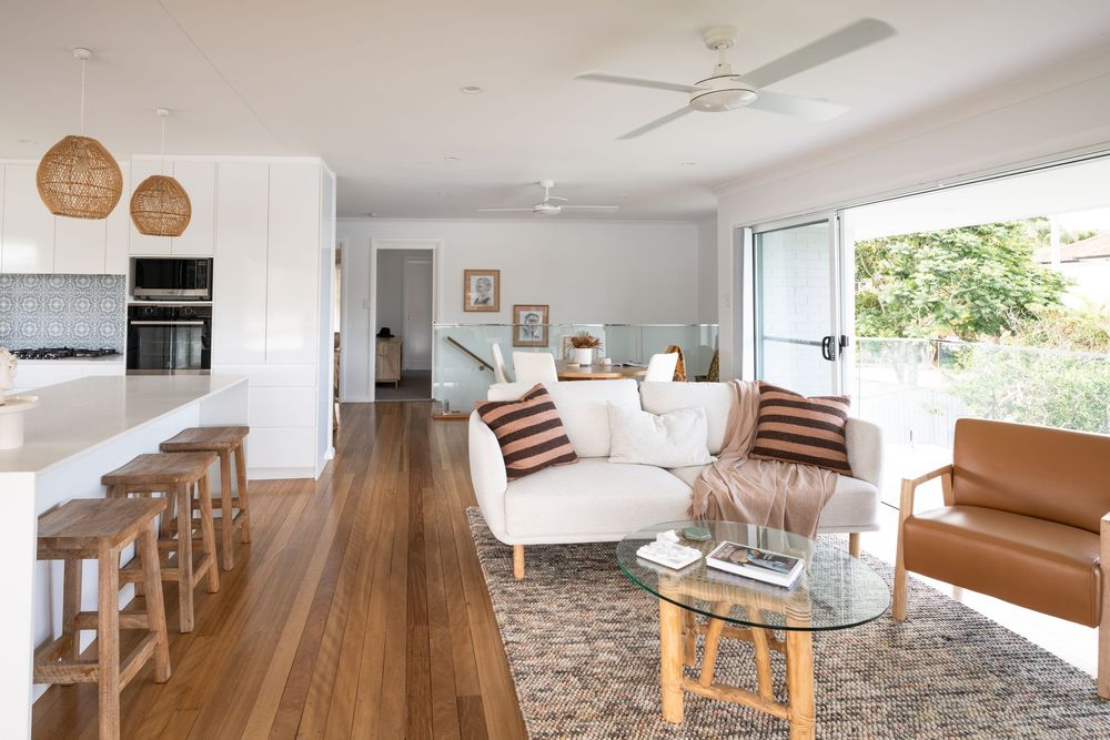 Modern coastal living room with hardwood floors, white sofa, tan leather chair and rattan pendant lights in open concept space.