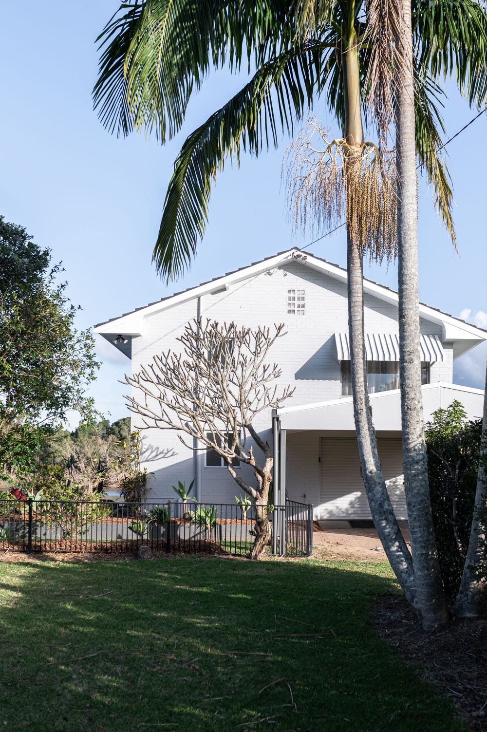 Modern white house with palm trees and manicured lawn features angled architectural elements and tropical landscaping.