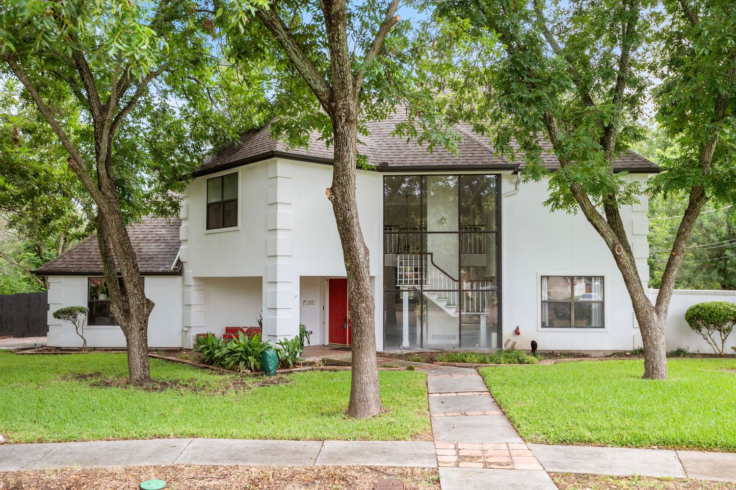 Modern white two-story house with tall windows and mature trees in the front yard.