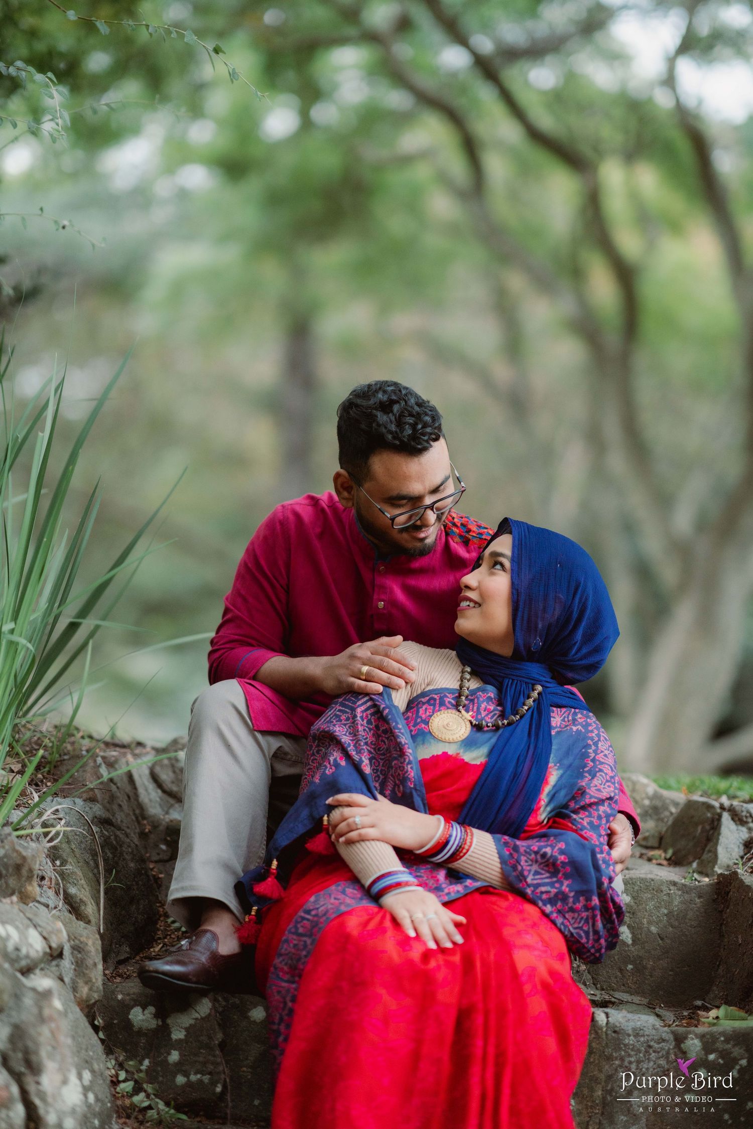 A couple poses together on tree roots in a park during their romantic outdoor photoshoot.