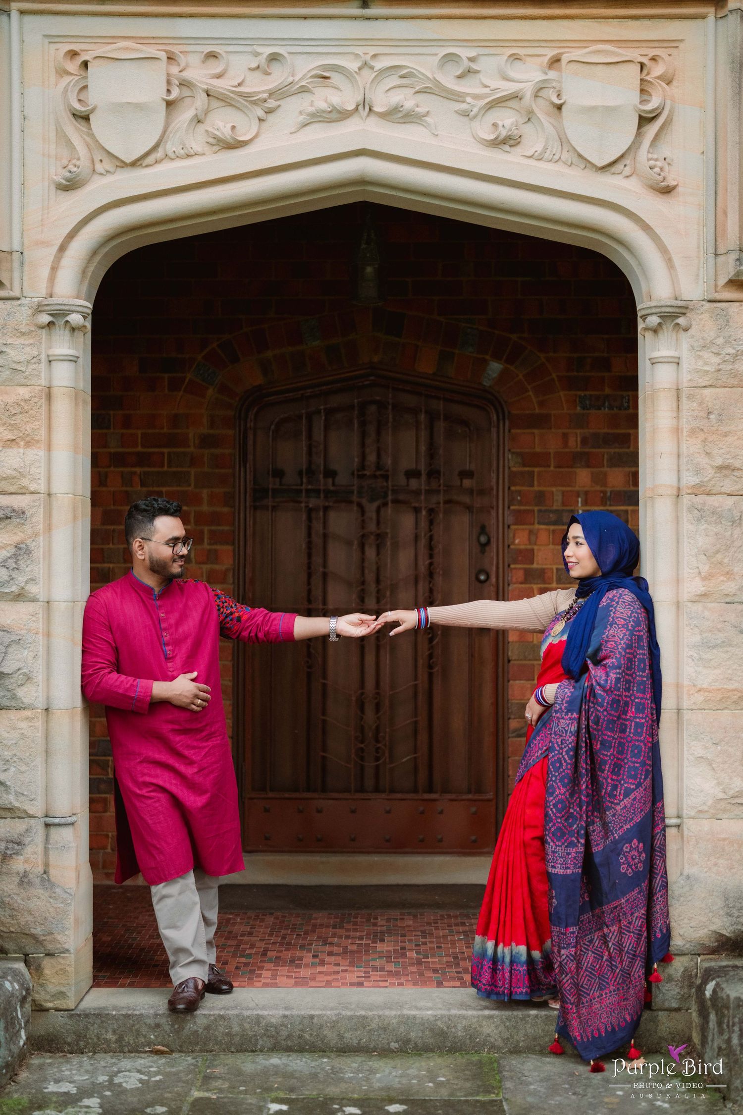 A romantic photoshoot in front of ornate stone archways featuring traditional South Asian attire in vibrant colors.