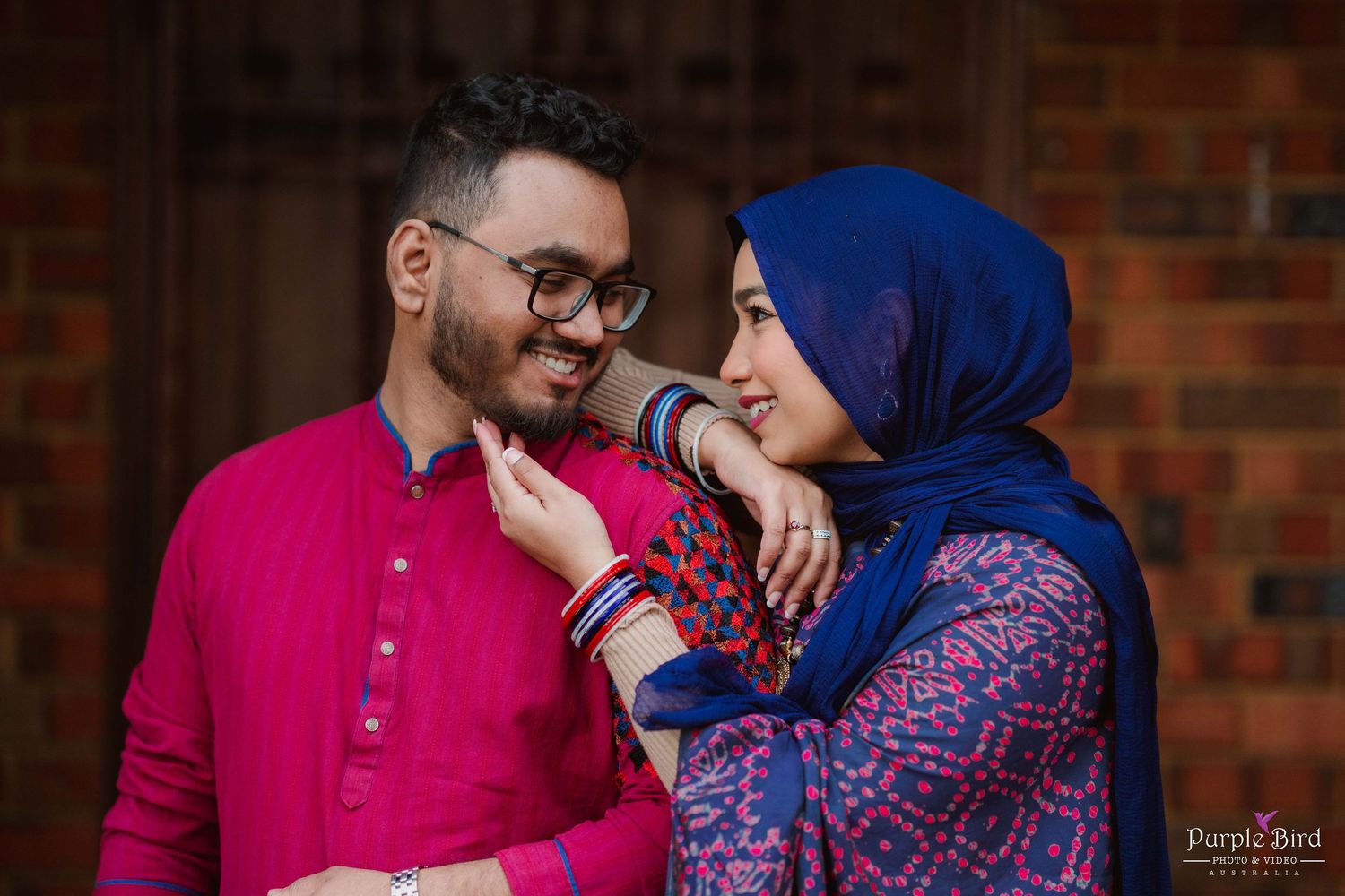 A couple shares an intimate moment against a brick wall background during their photo session.