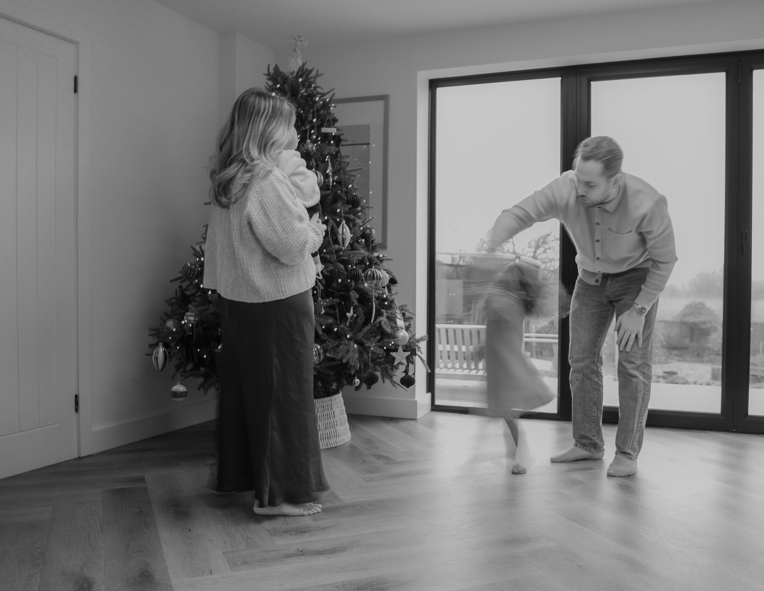 a black and white photo of a family dancing and having fun next a Christmas tree