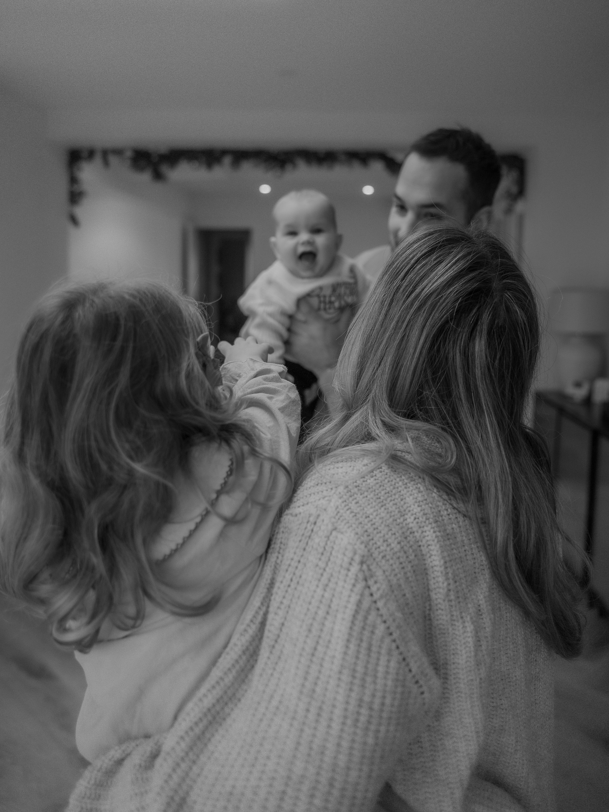 A series of black and white photos showing a person in a sweater interacting with a baby in candid moments.