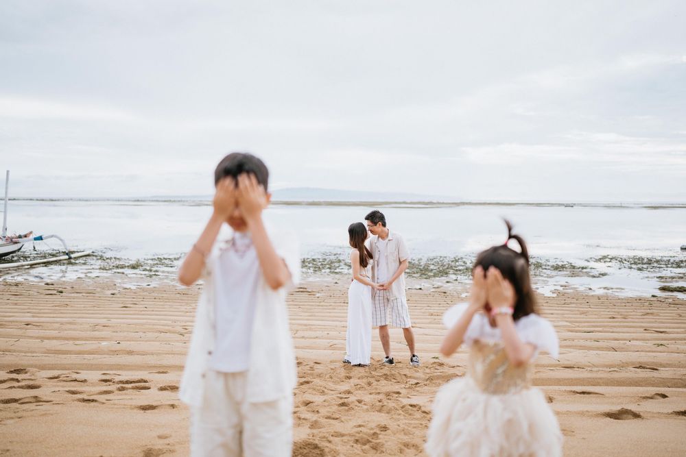 Family moment captured on a sandy beach with playful children in white outfits.