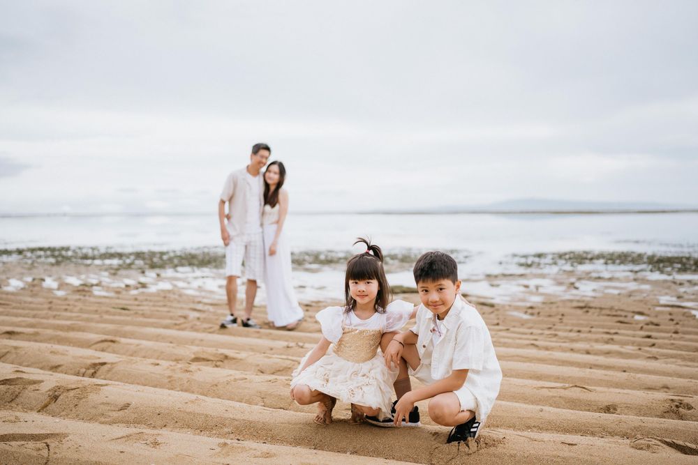 Family portrait on a sandy beach with children sitting in the foreground.