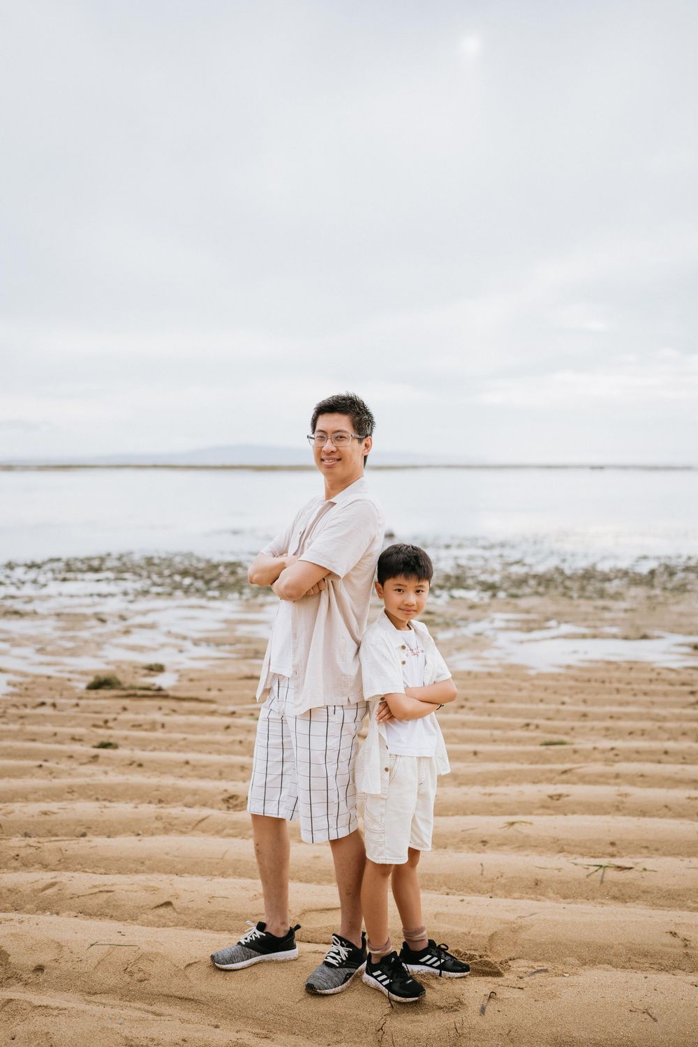 Two people in casual white outfits stand back-to-back on a textured sandy beach.