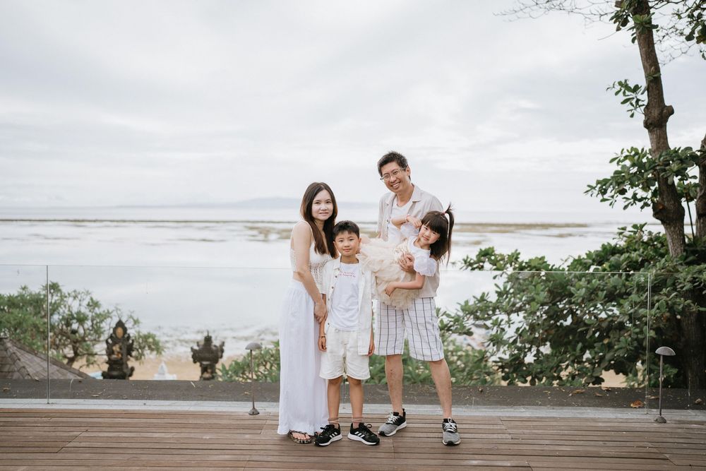 A family of four wearing coordinated white outfits poses on a wooden deck by the ocean.