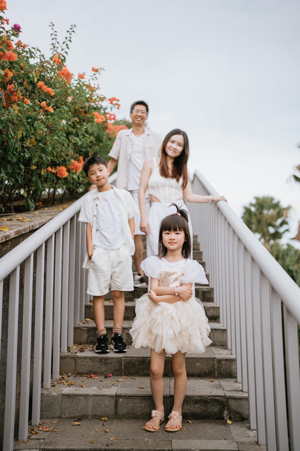A family poses on concrete steps with orange flowering bushes and metal railings.