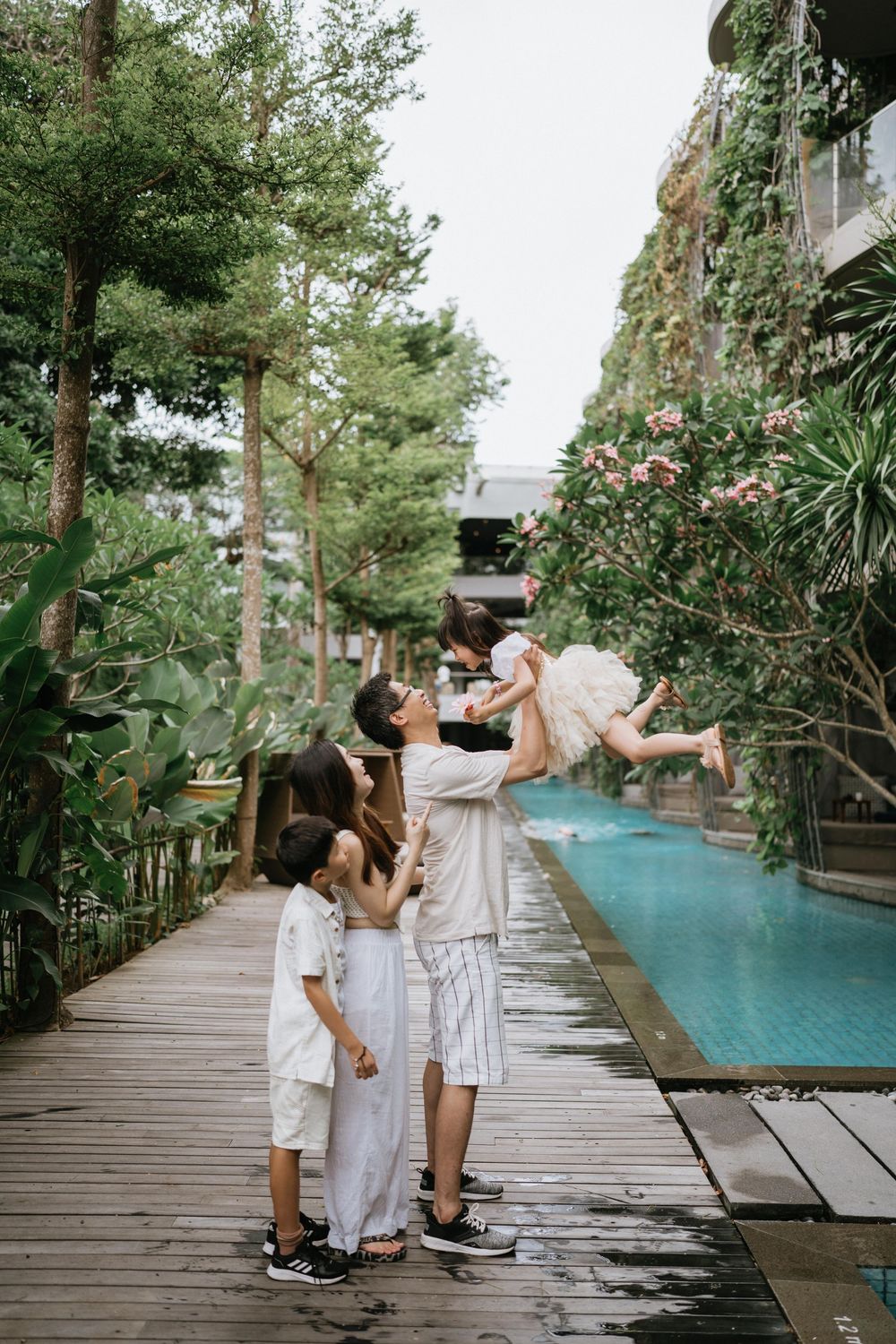 Family shares joyful interactions on wooden walkway near resort swimming pool.