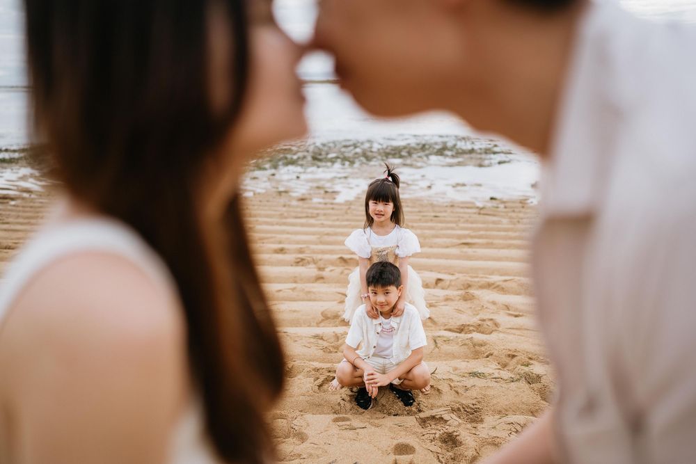 Children playing on a beach while a couple shares an intimate moment in the foreground.