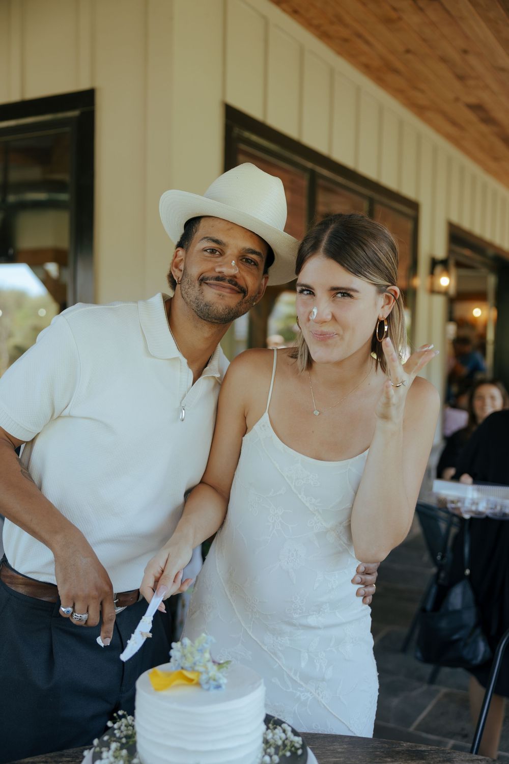Couple in white outfits share a playful moment at an outdoor reception venue.