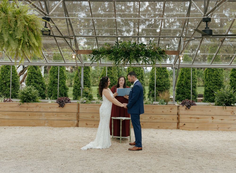 Wedding ceremony setup in an indoor greenhouse space with natural lighting and wooden elements.