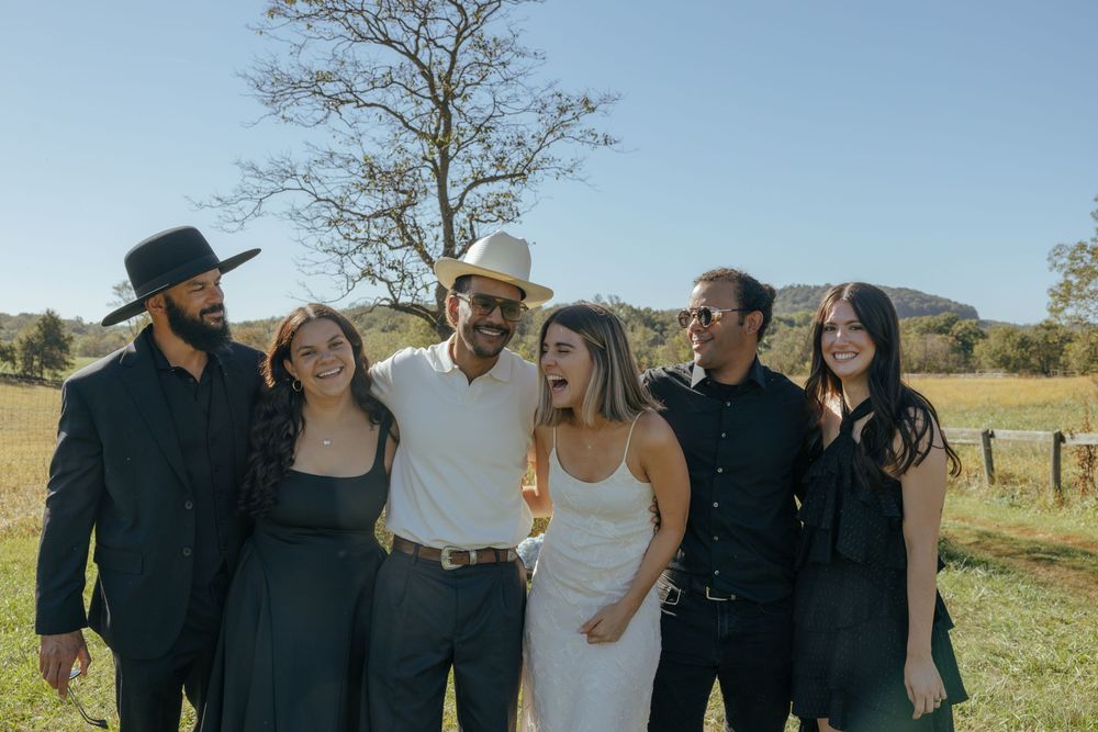 Group photo of wedding guests gathered outside on a sunny day in formal attire.
