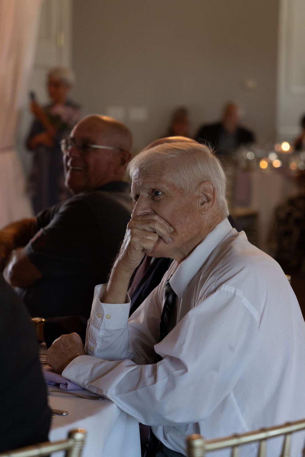 A person in white attire sitting and showing a sequence of emotional reactions while watching something offscreen.