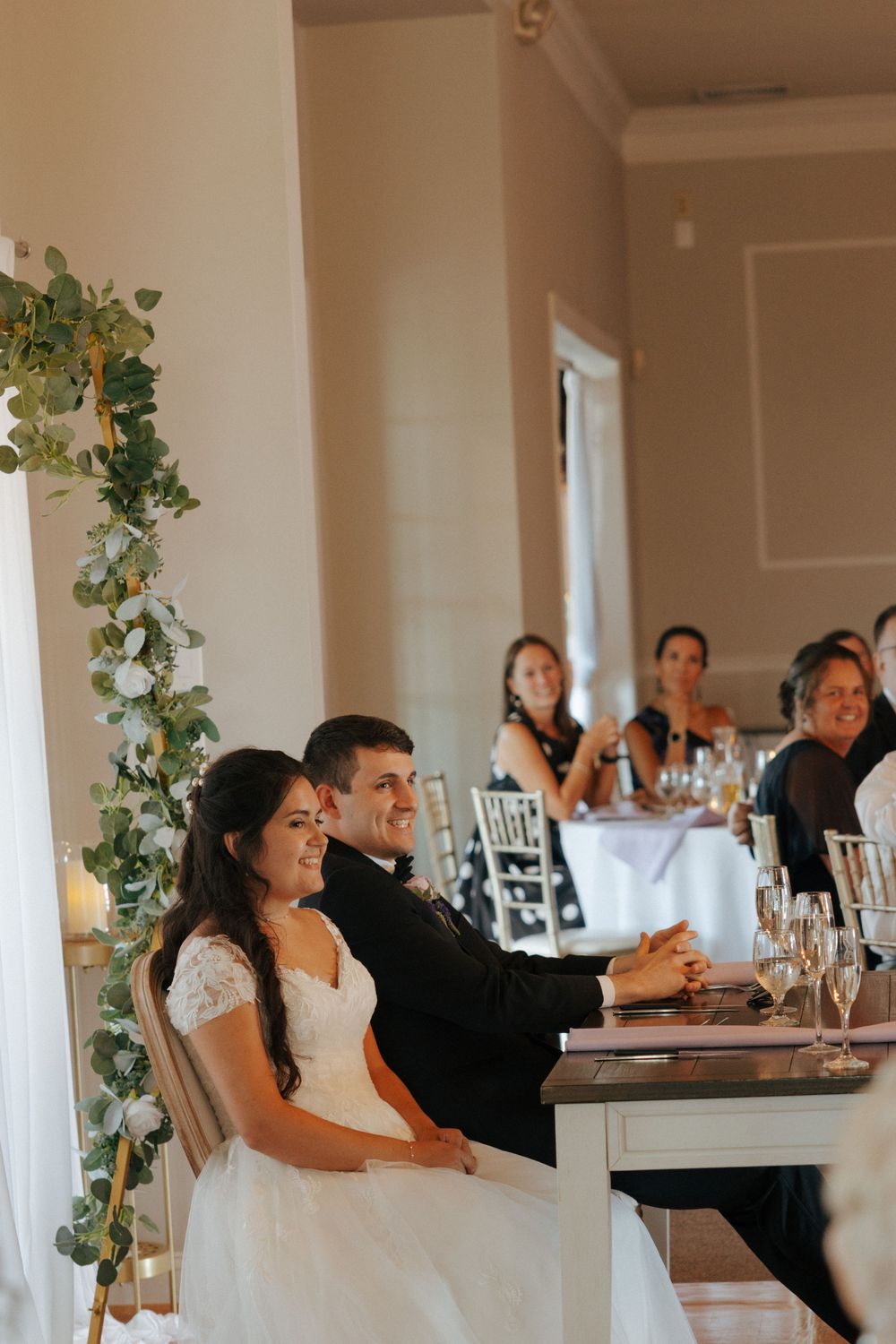 Wedding guests reacting emotionally during reception speeches at an elegant indoor venue decorated with greenery.
