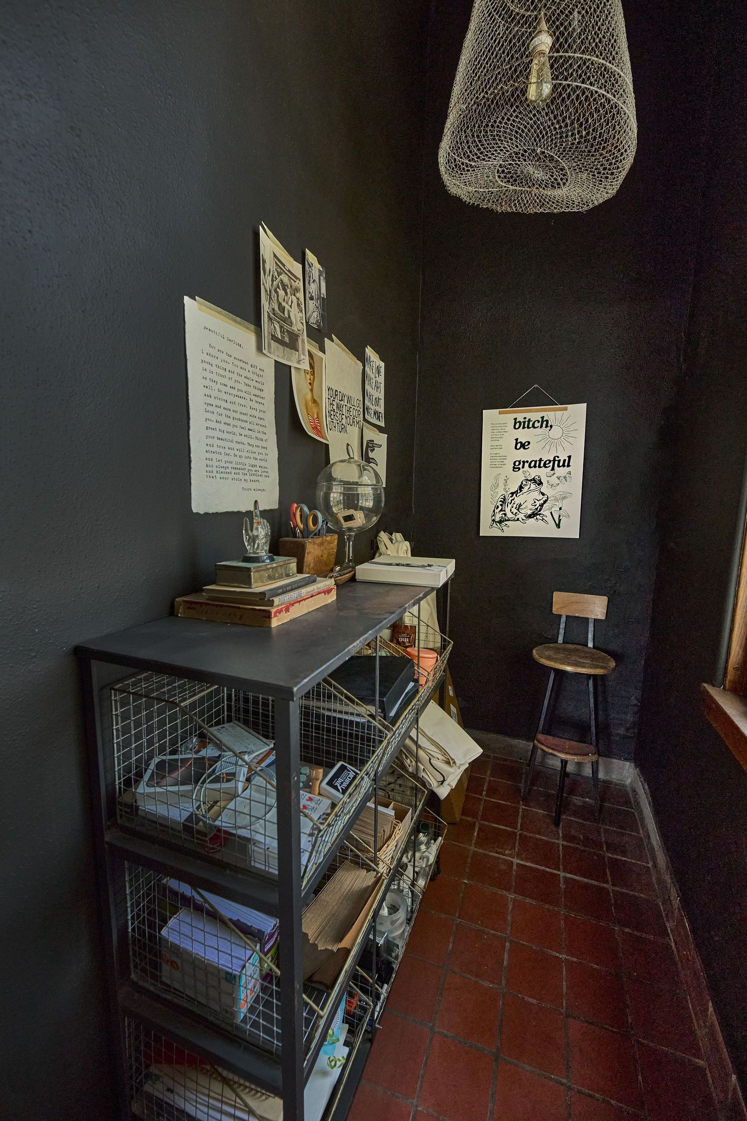 Dark room with wire storage shelves, terracotta floor tiles, and papers posted on black walls.