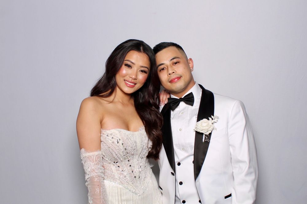 A couple poses together in formal wedding attire, including a white dress and black tuxedo with bow tie.