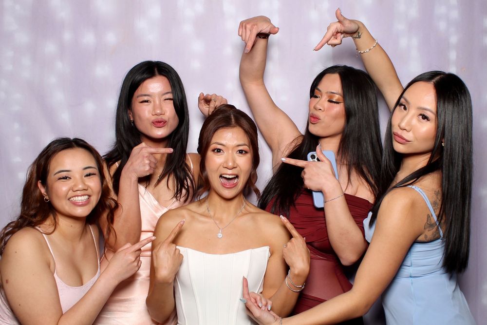 A group of elegantly dressed guests pose together at a festive celebration with sparkly backdrop lighting.