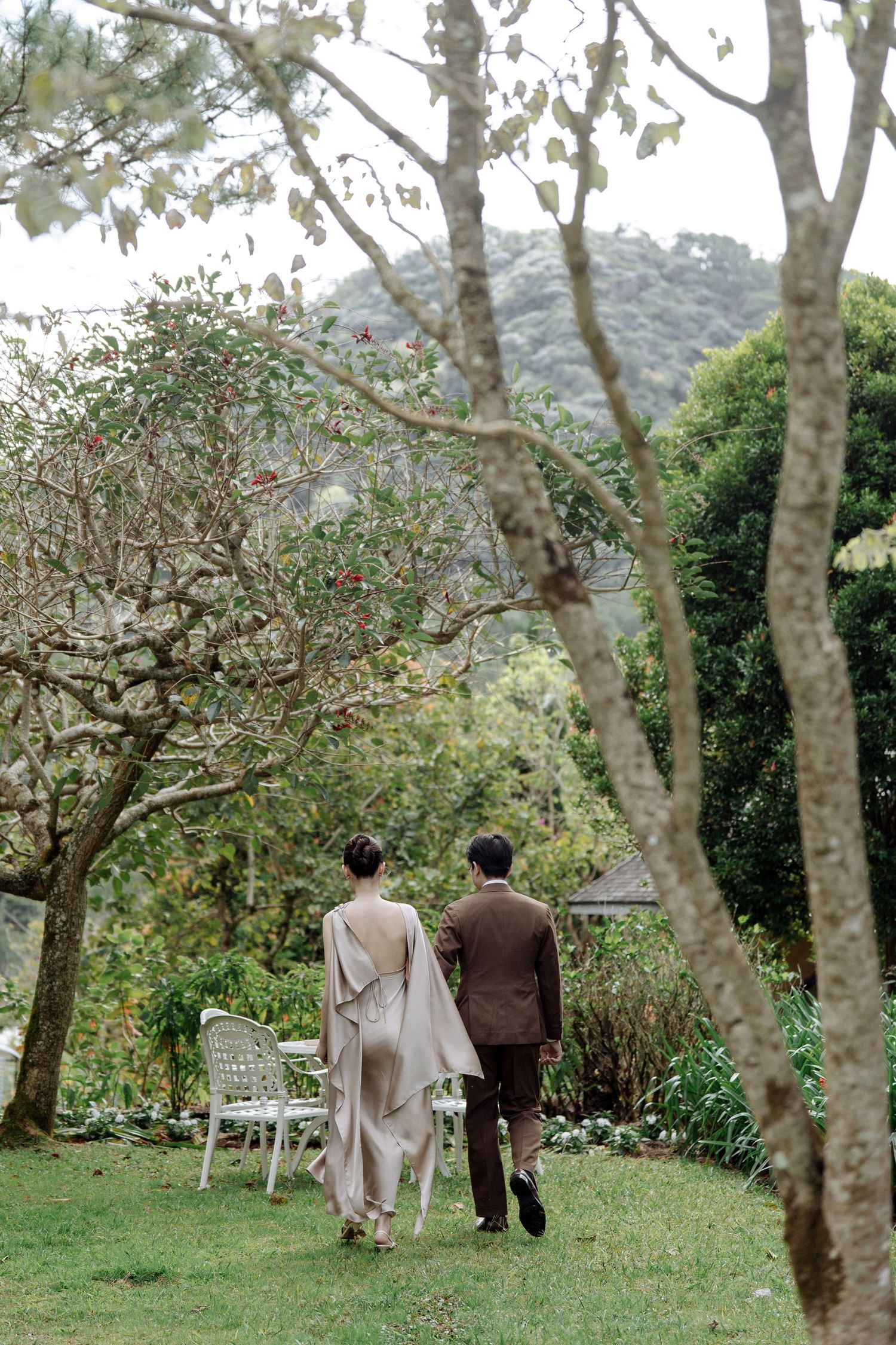 Couple walking hand in hand through a serene garden with mountain views.