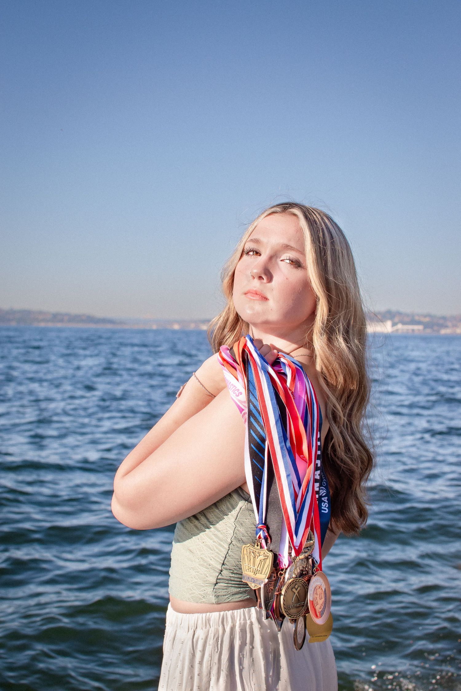 Senior girl holding a collection of gymnastics medals during her Alki Beach senior photo session in Seattle.