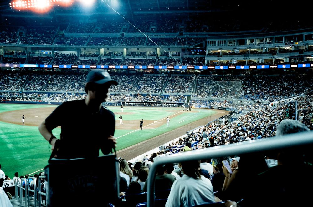 Panoramic view of a packed baseball stadium with fans watching a game under stadium lights during evening hours.