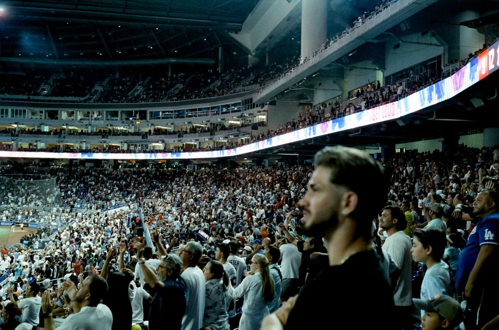 Spectators fill multiple levels of seating at a modern baseball stadium during a live game.