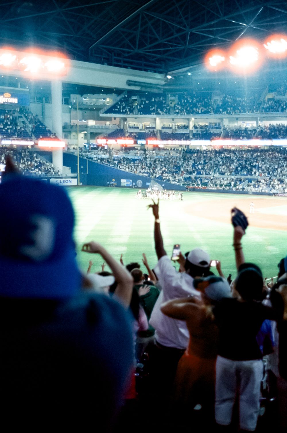 Sports fans cheer enthusiastically in a packed stadium with bright lights illuminating the field.