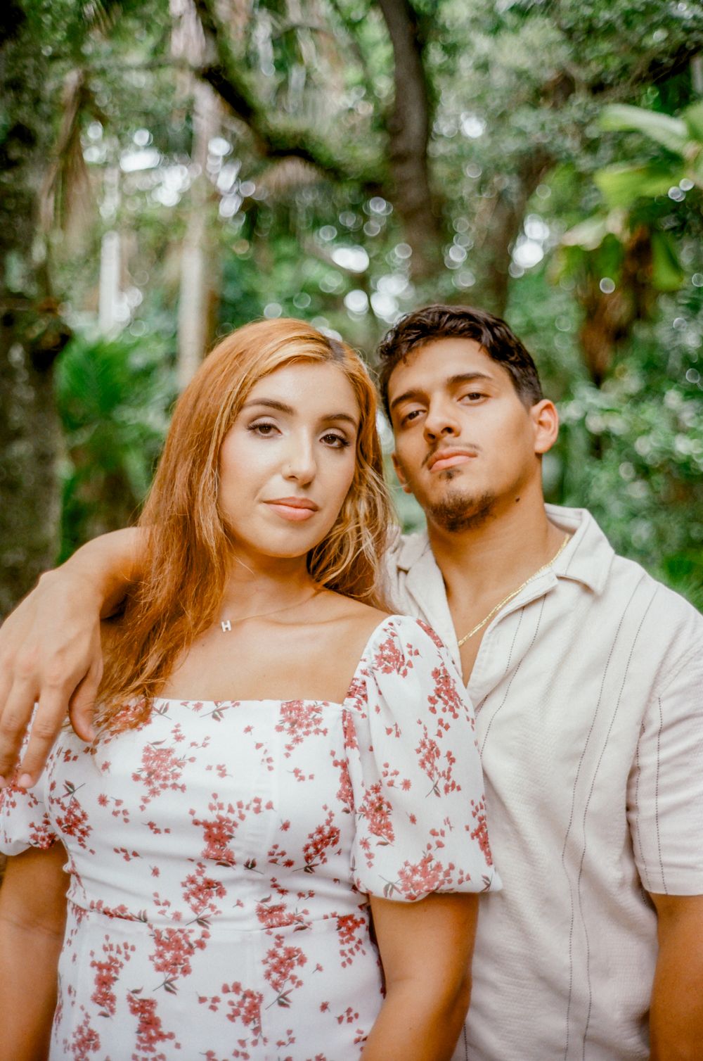 A couple poses together in a lush, wooded forest setting.