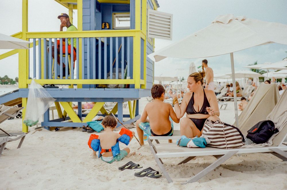 People relaxing on beach chairs near yellow lifeguard towers on a sunny beach day.