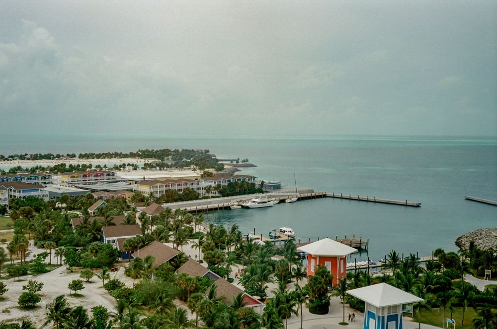 Panoramic aerial view of a coastal town with beachfront houses, docks, and turquoise waters stretching to the horizon.