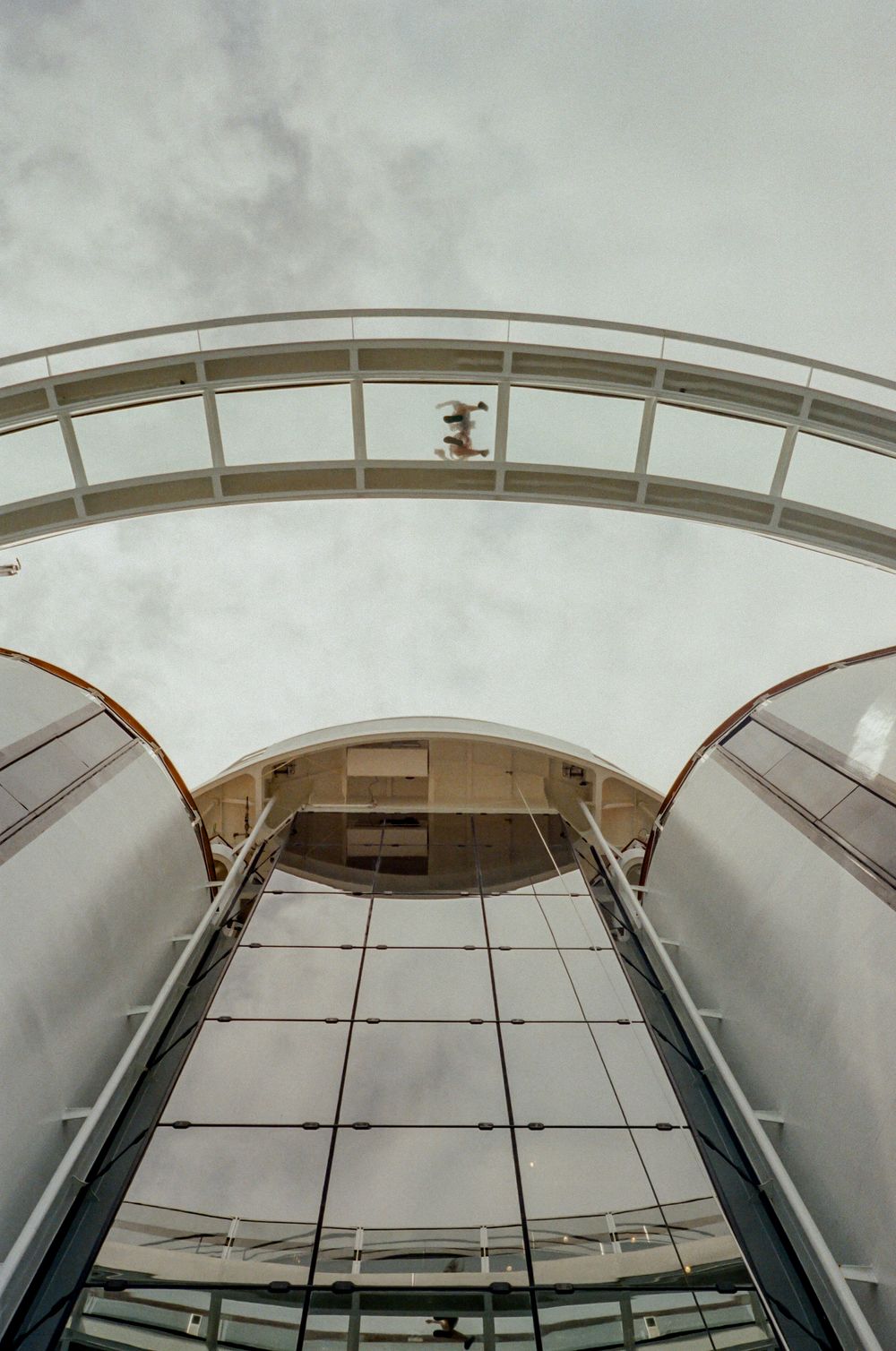 Low angle architectural view of curved glass roof panels creating geometric patterns against cloudy sky.