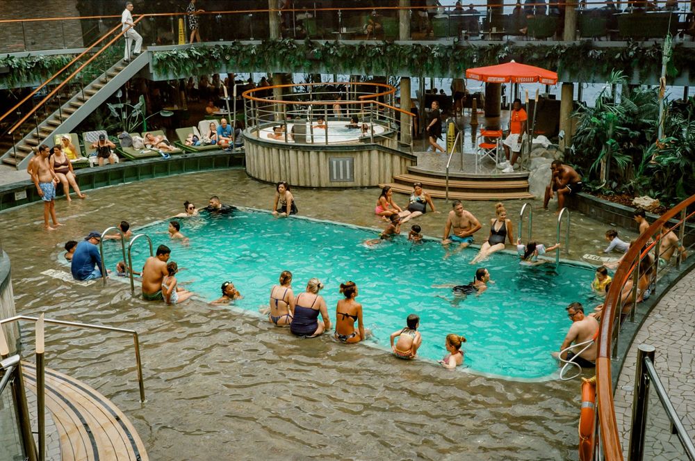 People swimming and relaxing in an indoor pool recreation center with multiple pools and lounge areas.