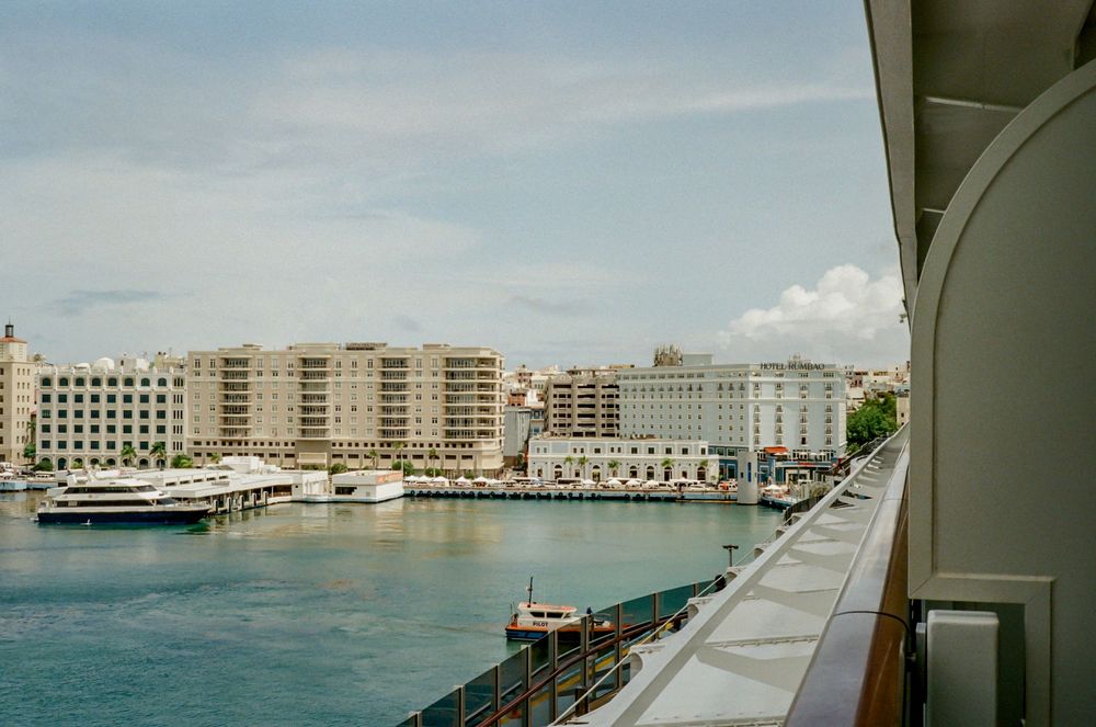 Panoramic view shows a multi-story beachfront hotel complex with curved architecture against a cloudy sky.