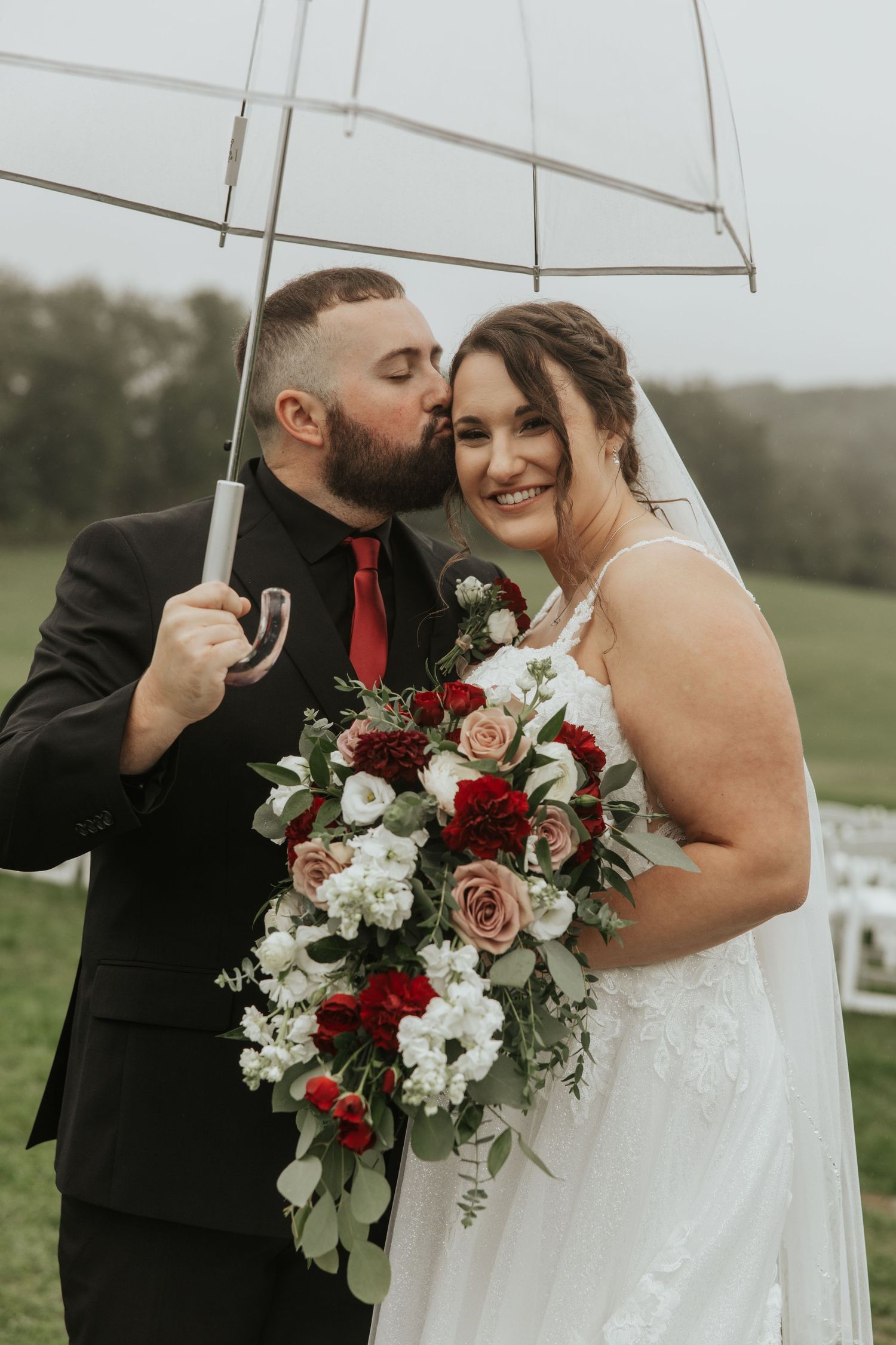 A romantic newlywed couple shares an intimate moment under a white umbrella in the rain on their wedding day.