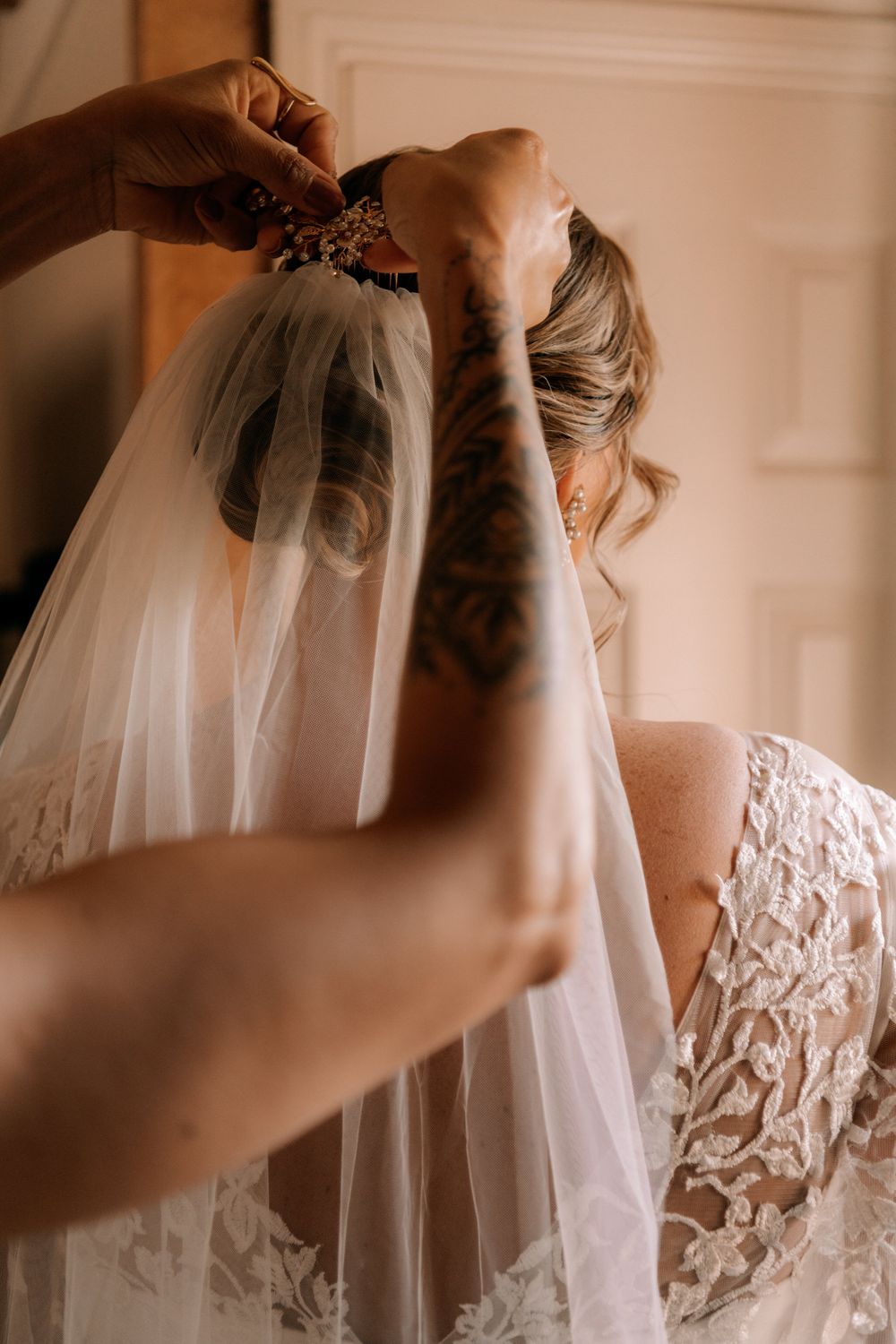 Attaching a delicate white wedding veil with floral lace trim to the back of a bridal hairstyle.