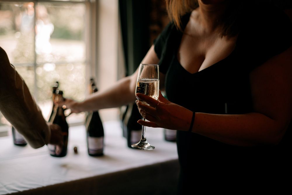 Two people enjoy drinks by a window, with sunlight filtering in as they hold wine glasses and bottles.