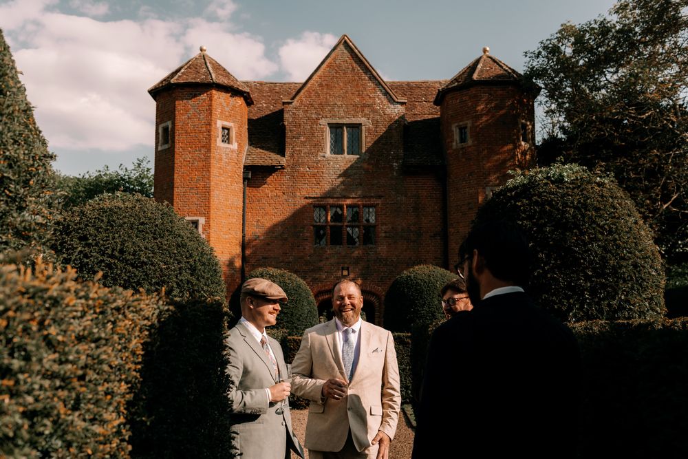 Group celebrating at an outdoor wedding reception near a rustic brick building on a sunny day.