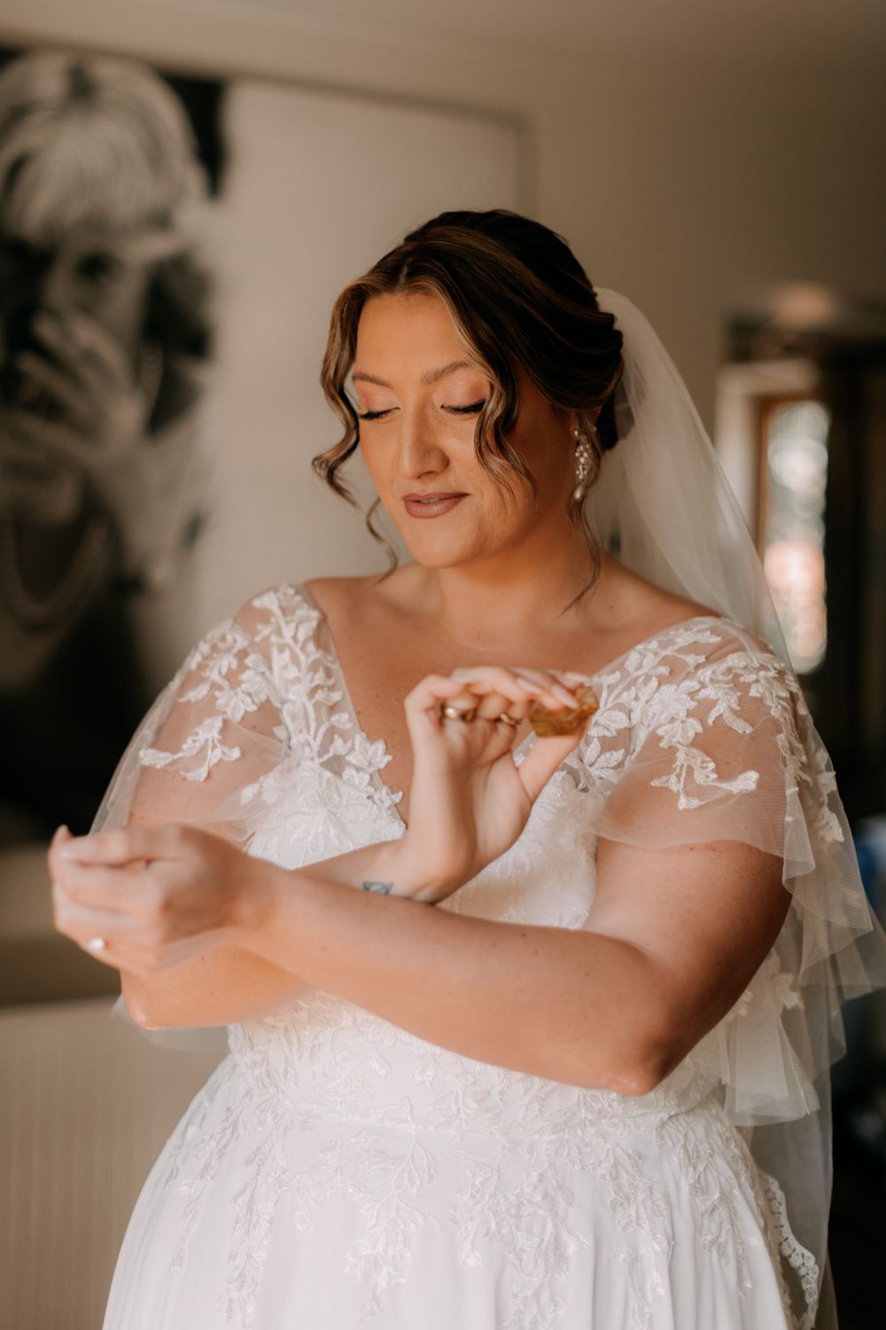 A bride in a lace wedding dress with fluttery cap sleeves looks down while getting ready on her wedding day.