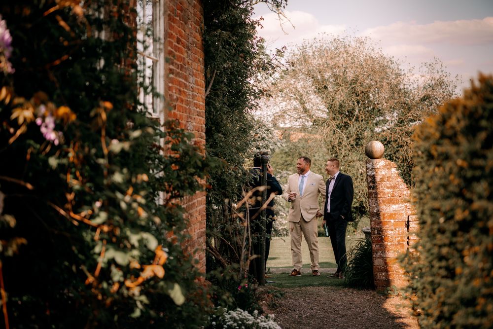 Enchanting garden pathway entrance is framed by brick pillars and blooming trees at sunset.
