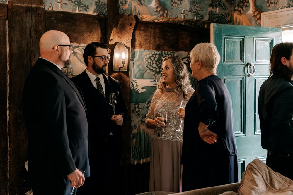 Wedding party members chat and mingle in a dimly lit venue before a special celebration.