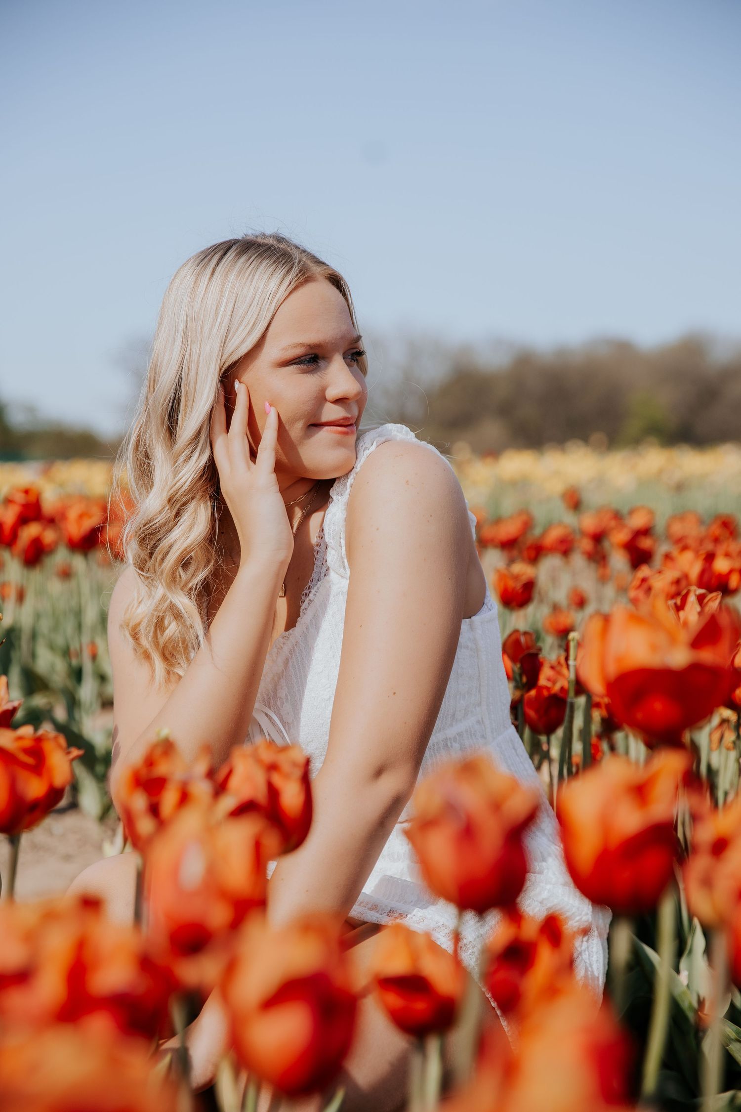 A beautiful spring scene features bright orange tulips with a woman in white enjoying the flower field.