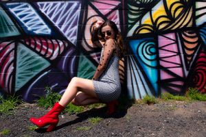 A model poses against a colorful geometric street art mural wearing red boots and a patterned dress.